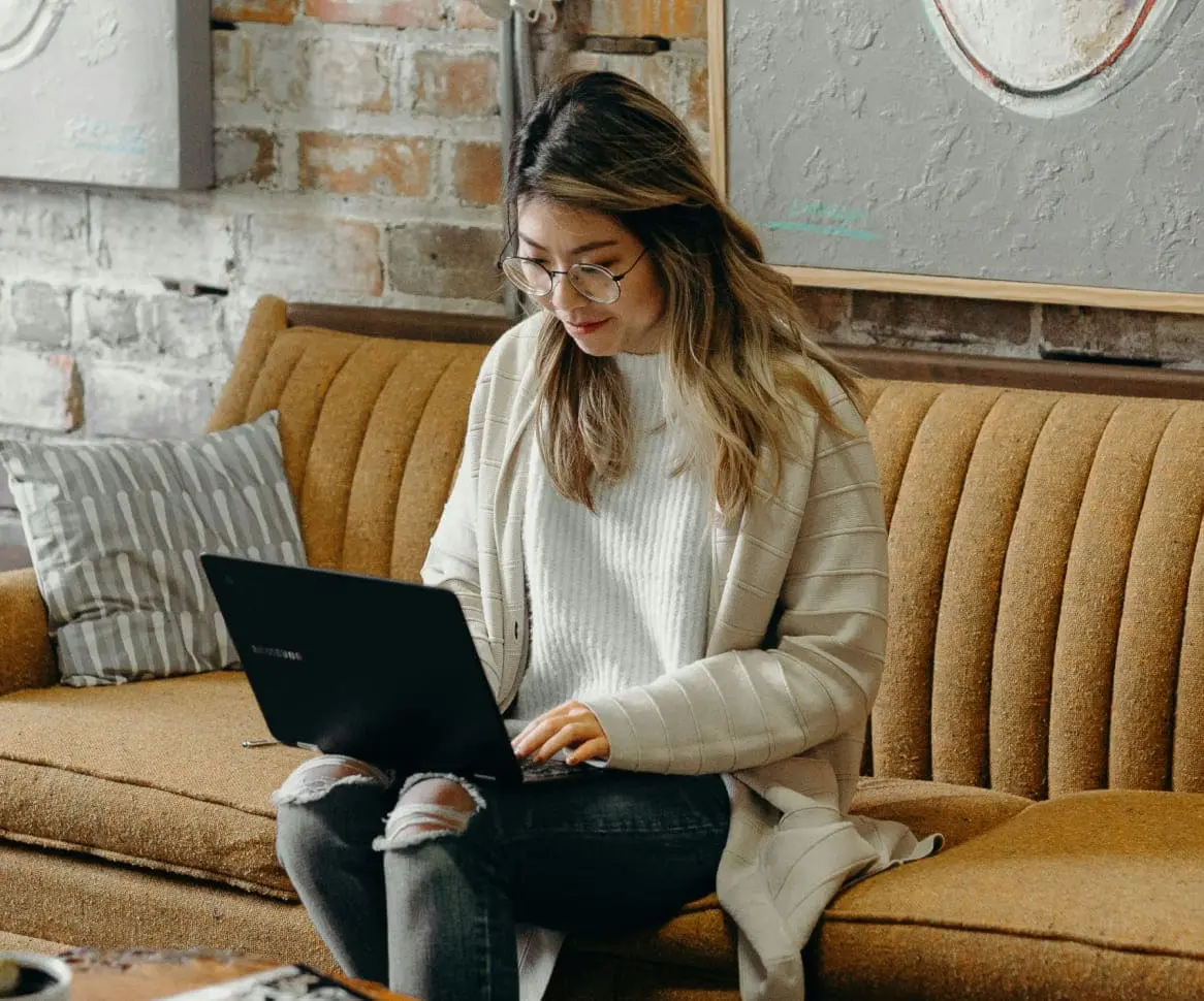 Studierende sitzt auf einer braunen a Couch und studiert mit ihrem Laptop auf dem Schoß