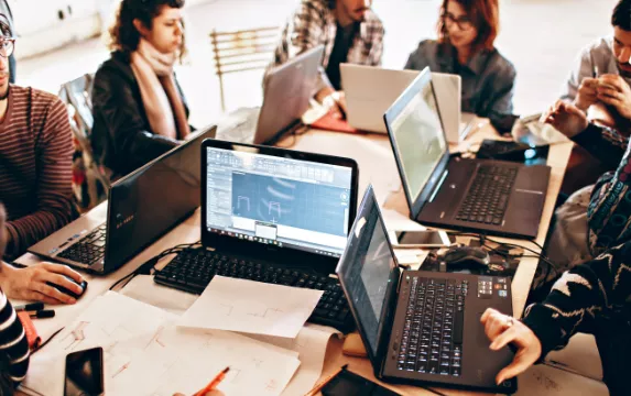 Eine Gruppe von Menschen sitzt mit Laptops an einem Tisch.